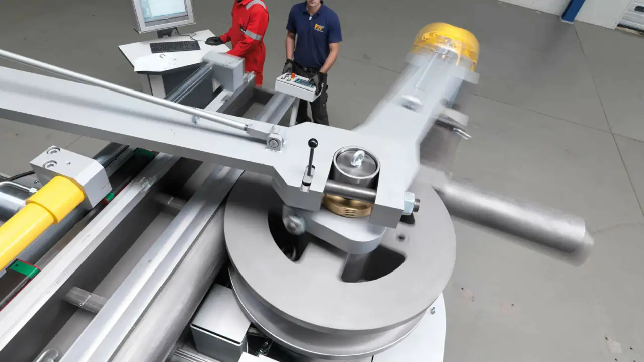 zwei Personen stehen vor sehr großer metallerner Industriemaschine, daneben Computer